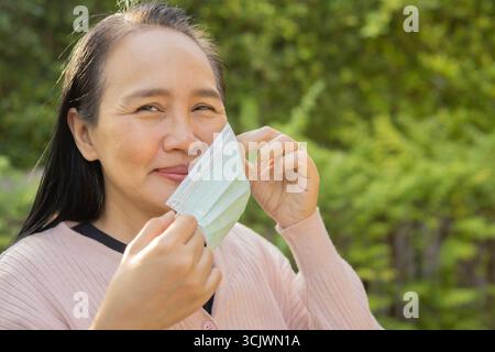 Felice positivo adulto Asain donna prende la maschera medica protettiva dal viso all'aperto. Concetto di protezione della salute. Foto Stock