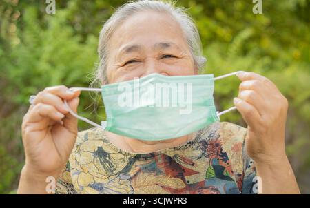 Primo piano ritratto di donna anziana felice che tiene la maschera medica all'aperto. Guardando la telecamera. Concetto di virus. Foto Stock