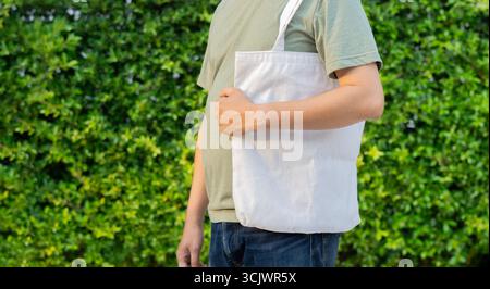 La vista ritagliata dell'uomo regge il tessuto di tela della borsa per un modello di mockup vuoto all'aperto nel parco. Concetto di riscaldamento globale. Foto Stock