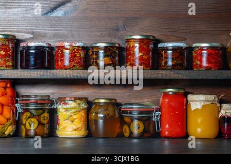 Molti cibi in scatola in vasetti di vetro su scaffali di legno in cantina per il consumo invernale, primo piano. Conservazione del cibo. Vaso colorato in salamoia e fermentato Foto Stock