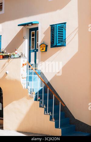 Scala colorata con gradini blu, cassetta postale gialla e bambole decorate su ringhiera alla luce del sole. Foto Stock