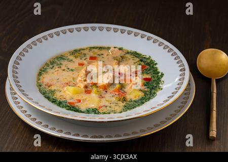 Zuppa fresca di pesce di salmone cremosa con patate, carote, broccoli, peperoni e cipolle in un piatto di ceramica su un tavolo di legno, da vicino. Una cena deliziosa Foto Stock