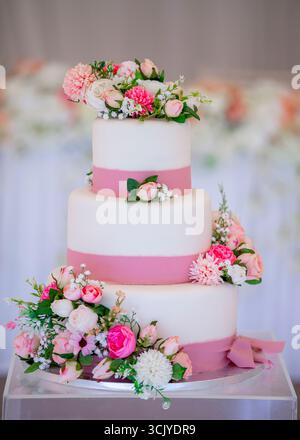 Elegante torta nuziale a tre piani decorata con delicati fiori rosa e bianchi, con un morbido nastro rosa Foto Stock