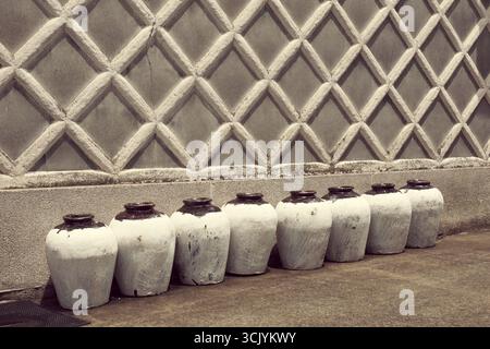 Fila di tradizionali bottiglie di sake giapponesi in ceramica vicino all'antico muro dell'edificio Foto Stock