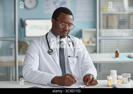 Uomo Nero di mezza età Dottore scrittura Note mediche in ufficio moderno Foto Stock