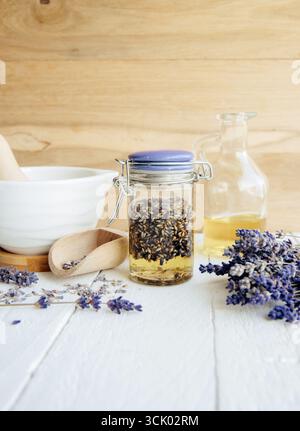 Olio di lavanda infuso a freddo fatto in casa. Olio d'oliva che ricopre i fiori di lavanda essiccati in un vaso di vetro. Mortaio e pestello, con un fascio di fiori di lavanda. Foto Stock