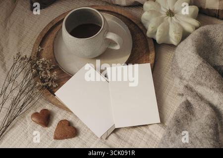 Accogliente appartamento autunnale con vista dall'alto. Biglietti d'auguri vuoti, mockup di invito, tazza di caffè in ceramica. Biscotti a forma di cuore, fiori secchi, zucca bianca Foto Stock