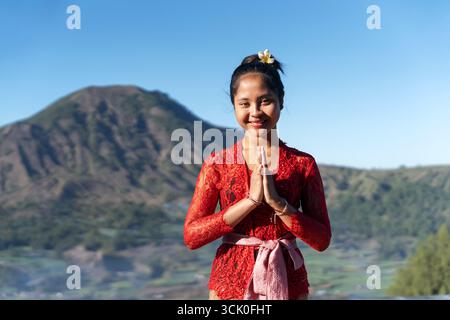 Ritratto di donna balinese mani aggrappato gesto di benvenuto con il Monte Vista Batur Foto Stock