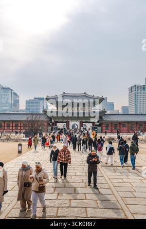 Seoul, Corea del Sud - 25 dicembre 2025: I visitatori camminano lungo il sentiero principale in pietra attraverso il Palazzo Gyeongbokgung verso il cancello, con i moderni grattacieli di Seoul Foto Stock