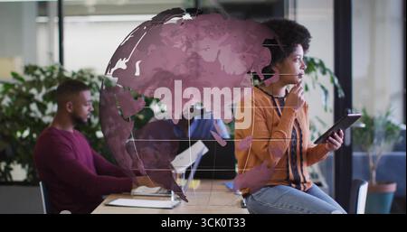 Tenendo in mano una donna tablet che indossa un cardigan senape che guarda la scrivania, con rivestimento a globo e spazio per copiare Foto Stock