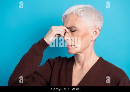 Donna matura con capelli grigi corti in posa ponderata su sfondo blu Foto Stock