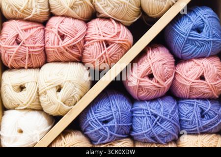 Le zecche di filettature per la maglia di colori diversi sono impilate sui ripiani, primo piano. Foto Stock
