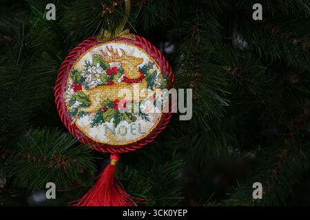 Ornamento natalizio Old World Holiday con cuciture incrociate su un albero di Natale. Questo ornamento natalizio rotondo con cervo e parola Noel ricamato e realizzato da Foto Stock