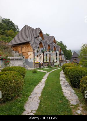 Fila di piccoli cottage in legno con tetti a punta, circondati da cespugli rifilati e sentieri in pietra. Turismo e alloggio in montagna in Serbia. Foto Stock