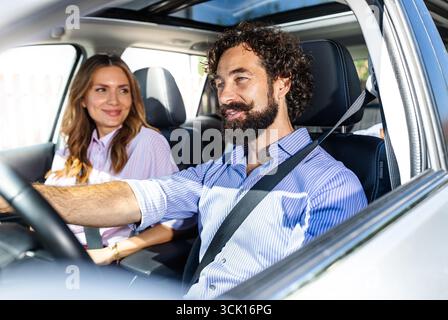 Coppia felice in vacanza. Bella donna che sorride sul sedile passeggero di suo marito mentre guida un'auto moderna Foto Stock