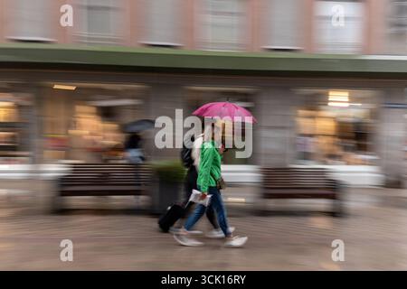 Frau mit pinkem Regenschirm in der Stadt 09.09.25, Limburgo: Symbolfoto, Illustrationsbild, Symbolbild, Illustrationsfoto, Alltagsszene Eine Frau geht bei Regen mit einem pinken Regenschirm und einer Grünen Jacke durch eine Einkaufsstraße. Neben ihr läuft eine weitere person mit Koffer. Durch die Bewegungsunschärfe entsteht Dynamik und ein lebendiger urbaner Eindruck. Limburg Hessen Deutschland *** donna con ombrello rosa in città 09 09 09 25, Limburg Symbol Photo, immagine illustrazione, immagine simbolo, foto illustrazione, scena di tutti i giorni Una donna cammina attraverso una strada dello shopping sotto la pioggia con un pi Foto Stock