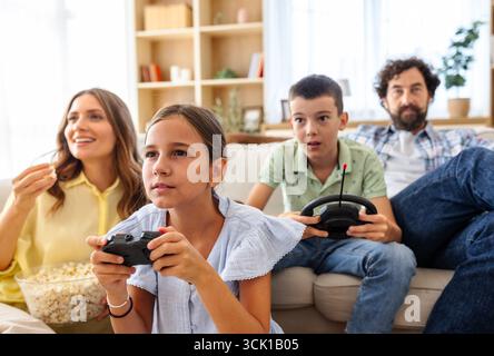 La famiglia si riunisce nel proprio soggiorno, divertendosi a giocare ai videogiochi insieme, mentre si gusta popcorn e spuntini in una casa accogliente Foto Stock