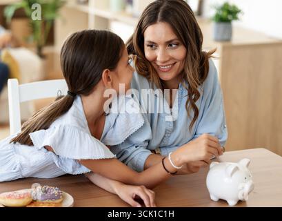 Madre e figlia condividono momenti di gioia risparmiando denaro nel salvadanaio di casa. Apprezzano il loro tempo insieme per i dessert Foto Stock