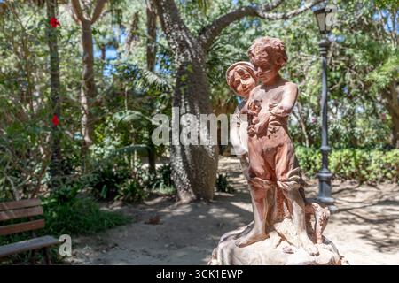 Statua di bronzo dei bambini nel parco ombreggiato circondato da alberi. Cadice, Andalusia, Spagna, settembre 2025. Foto Stock