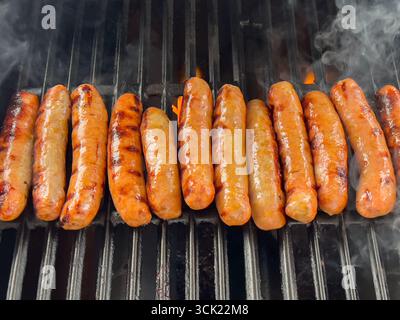 Salsicce grigliate con fumo che sale sul barbecue Foto Stock
