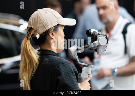Monaco di Baviera, Germania - 9 settembre 2025: Una donna filma con una tecnologia di stabilizzazione professionale DJI Ronin per registrazioni video fluide. *** Eine Frau filmt mit einem DJI Ronin Gimbal professionelle Stabilisierungstechnik für ruhige Videoaufnahmen Foto Stock