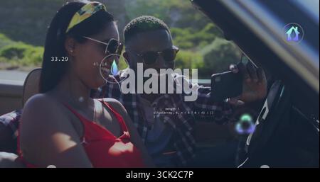 Coppia sorridente che indossa occhiali da sole per scattare selfie in beige convertibile su strada rurale, smartphone Foto Stock