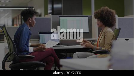 Due donne in abiti da lavoro che collaborano con documenti stampati e caffè in un ufficio open space Foto Stock