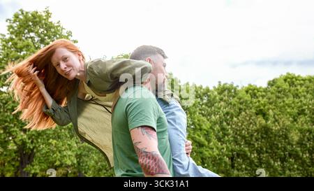 Un uomo e una donna condividono un momento di gioia in un parco, mostrando energia giocosa. La donna è sollevata dall'uomo, creando una composizione dinamica e vivace. TH Foto Stock