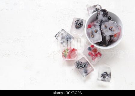 Ciotola con frutti di bosco congelati in cubetti di ghiaccio su sfondo bianco Foto Stock