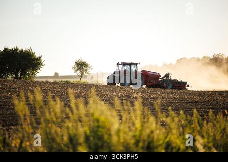 Moderno trattore agricolo con seminatrice su campi polverosi durante l'estate, seminando nuovi raccolti per la prossima stagione. Macchine agricole per la preparazione del terreno e la semina Foto Stock