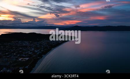 Vista aerea della luce dorata che bacia la tranquilla costa mentre il crepuscolo dipinge il cielo sopra le acque calme vicino a Campeche, Florianópolis, Santa Catarina, Brasile. Foto Stock