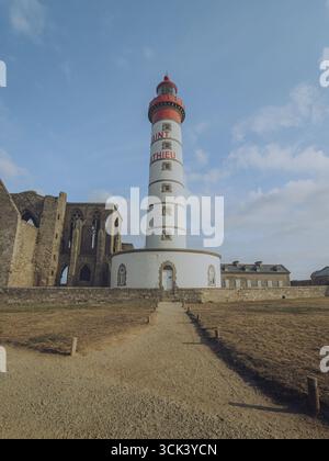 La vista del suggestivo faro di Phare de Saint-Mathieu, con la sua cima rossa e il corpo bianco, si erge alto accanto alle rovine dell'abbazia, Plougonvelin, Bretagne, Francia. Foto Stock