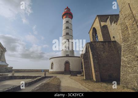La vista del suggestivo faro Phare de Saint-Mathieu, con la sua audace cima rossa, si erge alto contro le antiche rovine di pietra, un faro costiero a Plougonve Foto Stock