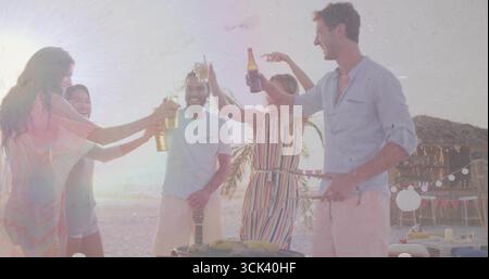 Amici che allevano bottiglie di birra e tostano barbecue sulla spiaggia del tramonto, con grill e luci a corda Foto Stock