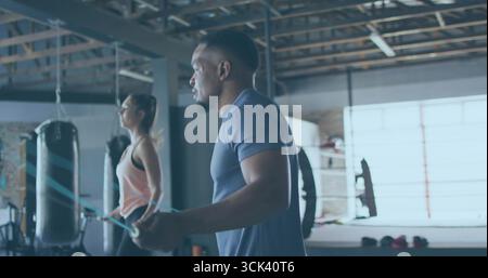 Salta un uomo che indossa maglietta e pantaloncini navy con corda per saltare nella palestra di pugilato, con borse da pugno Foto Stock