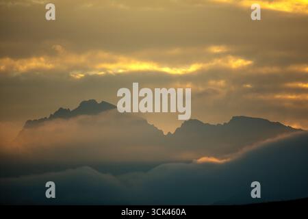 Vista delle maestose montagne avvolte dalla nebbia eterea, bagnate dal caldo bagliore del sole che tramonta, creando un paesaggio sereno, Skardu, Gilgit Baltistan, Pakistan. Foto Stock