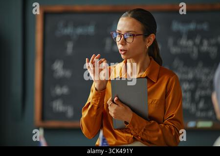 Giovane donna caucasica che spiega la lezione mentre tiene in mano un tablet digitale Foto Stock