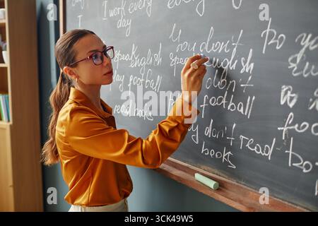 Giovane donna caucasica adulta che scrive frasi in inglese sulla lavagna in aula Foto Stock