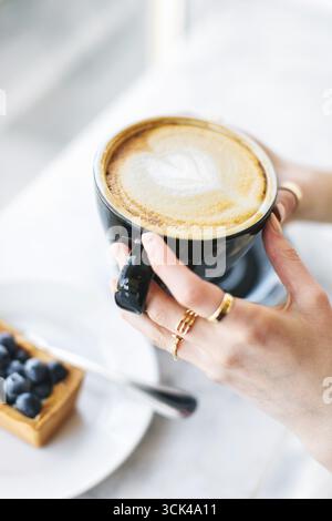 Cappuccino con motivo a base di schiuma di latte nelle mani delle donne Foto Stock