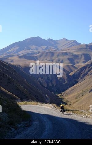 Un ciclista avventuroso percorre una strada sterrata nei monti Tian Shan del Kirghizistan. Foto Stock