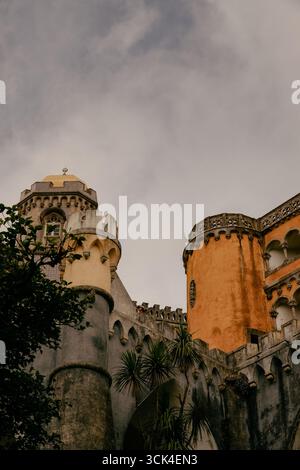 Vista architettonica del Palácio da pena a Sintra, Portogallo, con la sua cupola dorata, torri cilindriche gialle, contro un cielo nuvoloso. Foto Stock