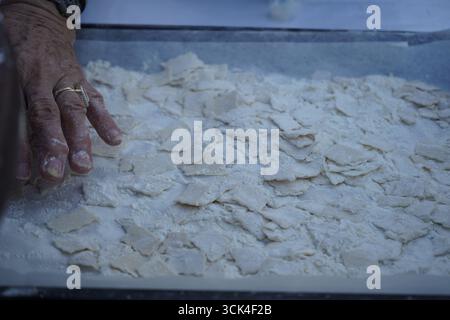 Mano di una donna anziana, con un dito di martello e un anello, che prepara la tradizionale pasta cretese mangiri su una superficie infarinata, un eccellente sfondo. Foto Stock
