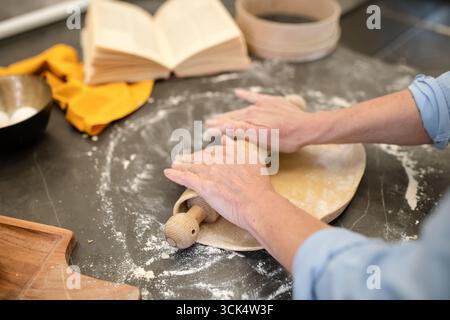 Le mani delle donne stendono l'impasto con un mattarello Foto Stock