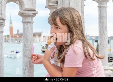 Una ragazza mangia il gelato mentre si siede su una ringhiera di pietra lungo un canale a Venezia Foto Stock