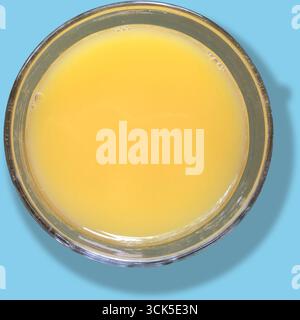 Una ciotola di vetro trasparente riempita di liquido giallo, magari una bevanda o un succo, che mostra il suo colore vivace e la consistenza liscia. Foto Stock