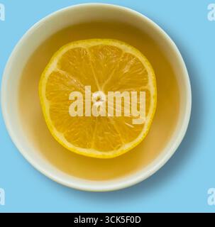 Una ciotola contenente una fetta di limone che galleggia in un liquido di colore chiaro, possibilmente tè o acqua, creando un aspetto rinfrescante. Foto Stock
