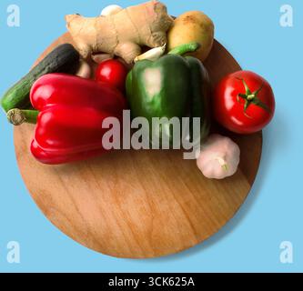 Un tagliere in legno espone una varietà di verdure fresche, tra cui peperoni, pomodori, cetrioli, aglio, zenzero e patate. Foto Stock