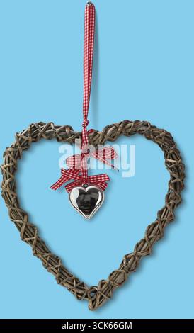 Una corona decorativa a forma di cuore fatta di ramoscelli, adornata da un nastro a scacchi rosso e bianco e da un piccolo cuore d'argento. Foto Stock