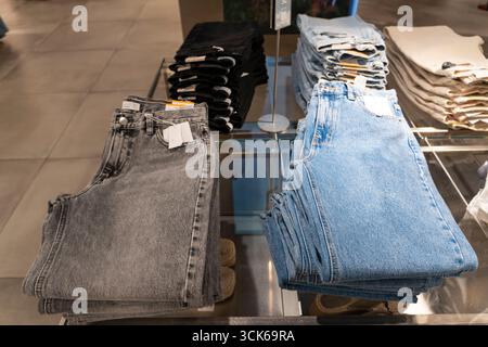 Pile di jeans blu disposte ordinatamente su scaffali di legno in un negozio di abbigliamento, che espone la moda al dettaglio e il concetto di merchandising Foto Stock