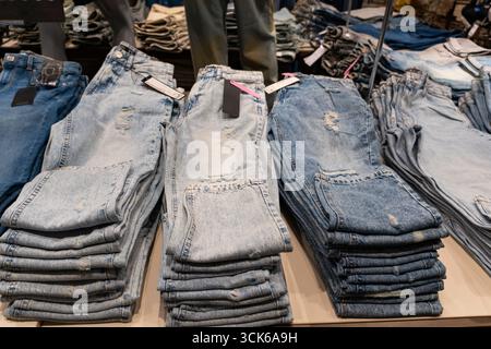 Pile di jeans blu disposte ordinatamente su scaffali di legno in un negozio di abbigliamento, che espone la moda al dettaglio e il concetto di merchandising Foto Stock
